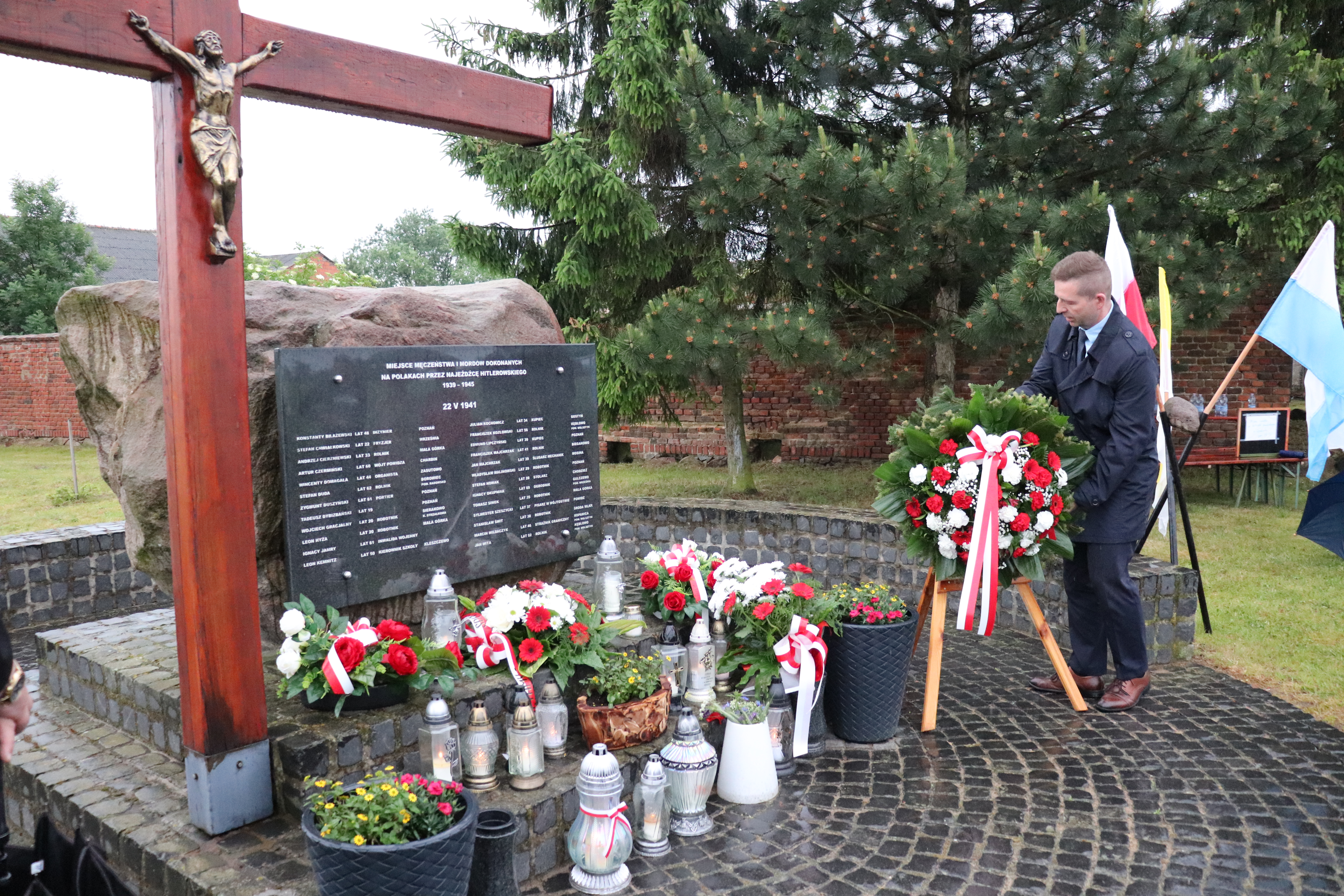 Pomnik – miejsce pamięci w Małej Górce. Duży głaz, na nim tablica z nazwiskami. Obok duży drewniany krzyż. Przed pomnikiem kwiaty i znicze. Obok Burmistrz wieszający na stojaku biało-czerwony wieniec kwiatów. 